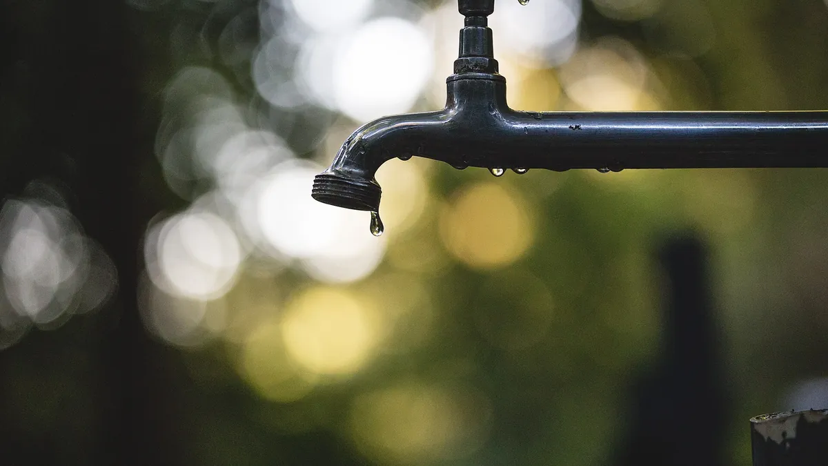 Outdoor metal water tap with a drop falling from the spout